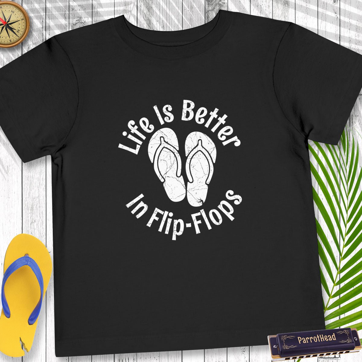 Black t-shirt with 'Life is Better in Flip-Flops' text and flip-flop graphics on a wooden surface.