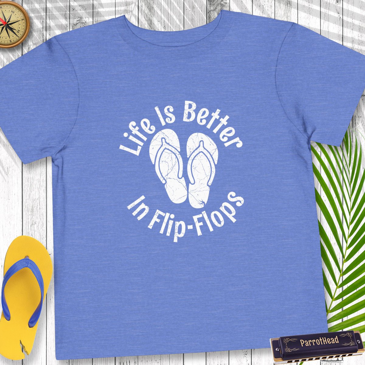 Blue t-shirt with 'Life Is Better In Flip-Flops' text and flip-flop graphic on a wooden surface.