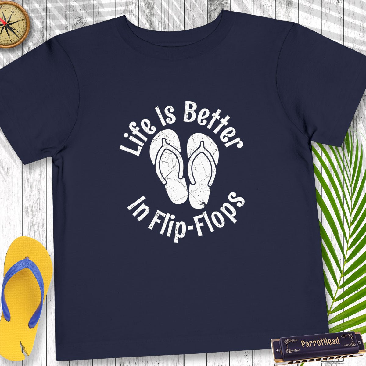 Navy blue t-shirt with 'Life is Better in Flip-Flops' text and flip-flop graphics on a wooden surface.