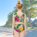 little girl wearing a colorful tropical leaf patterned swimsuit looking down a tropical resort island beach