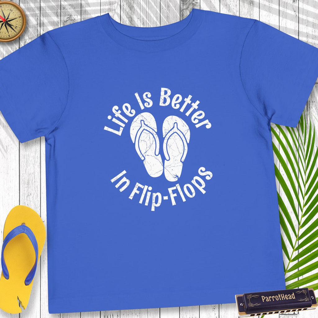 Blue t-shirt with 'Life Is Better In Flip-Flops' text and flip-flop graphics on a wooden surface.