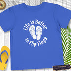 Blue t-shirt with 'Life Is Better In Flip-Flops' text and flip-flop graphics on a wooden surface.