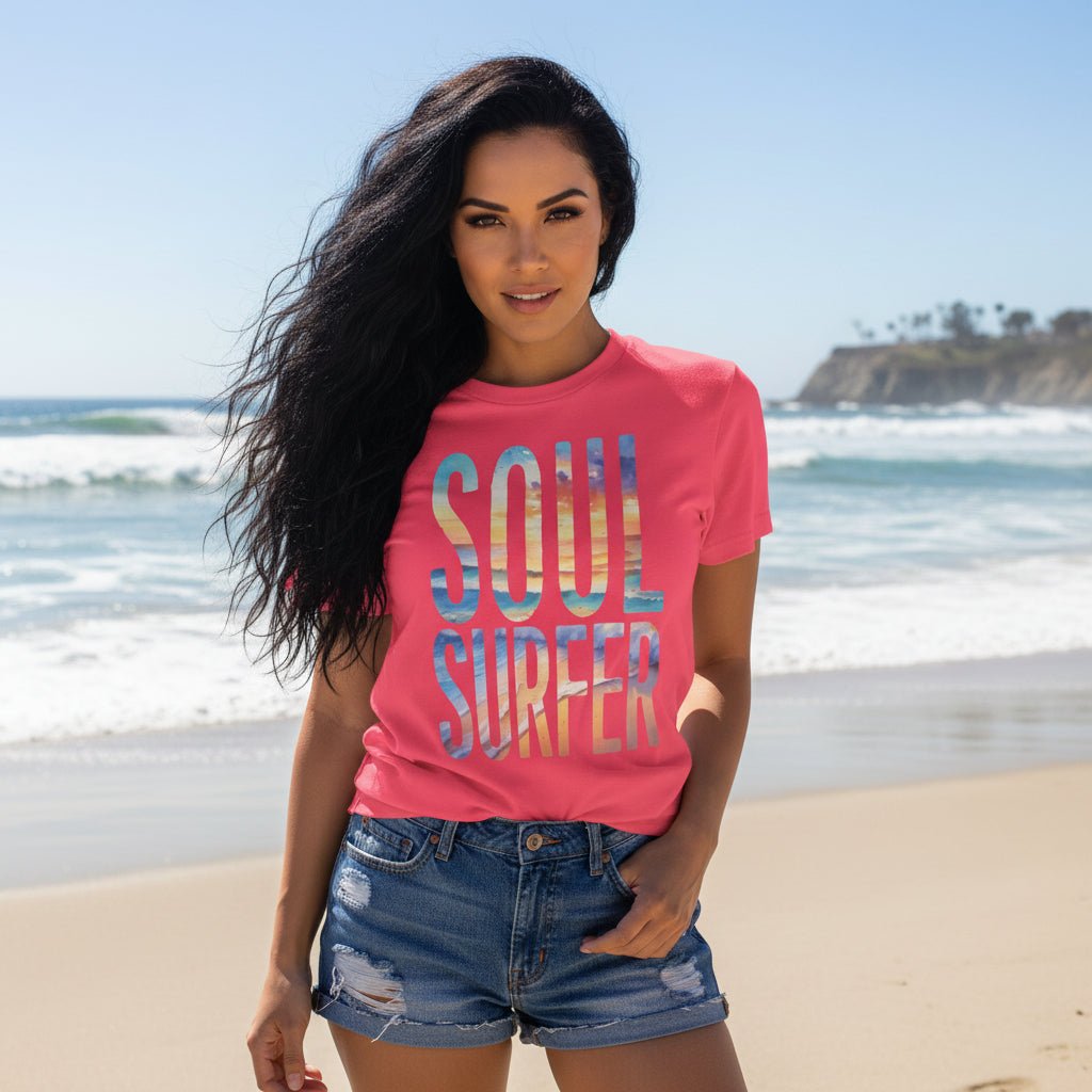 Beautiful woman wearing a bright pink short-sleeve t-shirt with a colorful graphic reading 'SOUL SURFER' in a watercolor-style beach scene of blue, yellow, and orange standing on La Jolla Beach