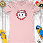 Pink t-shirt with a logo and text on a wooden surface with beach accessories.