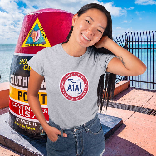 Woman wearing a t-shirt with a logo standing next to a large buoy by the water.