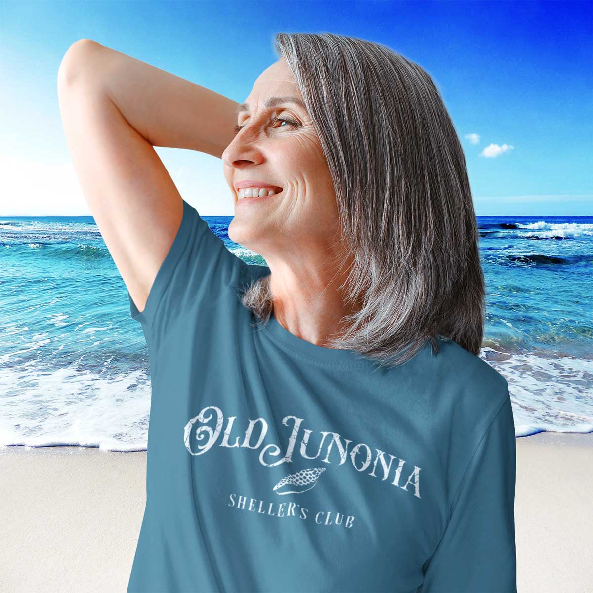 Woman wearing a blue t-shirt with 'Old Junonia Sheller's Club' text on a beach