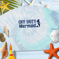 Light blue tie-dye crop tee with 'Off Duty Mermaid' print, surrounded by beach-themed decor.