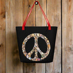 Black Tote Bag with a red strap hanging on a rustic wood wall in a seaside surf shack. Bag features Seashell art forming a Peace Sign