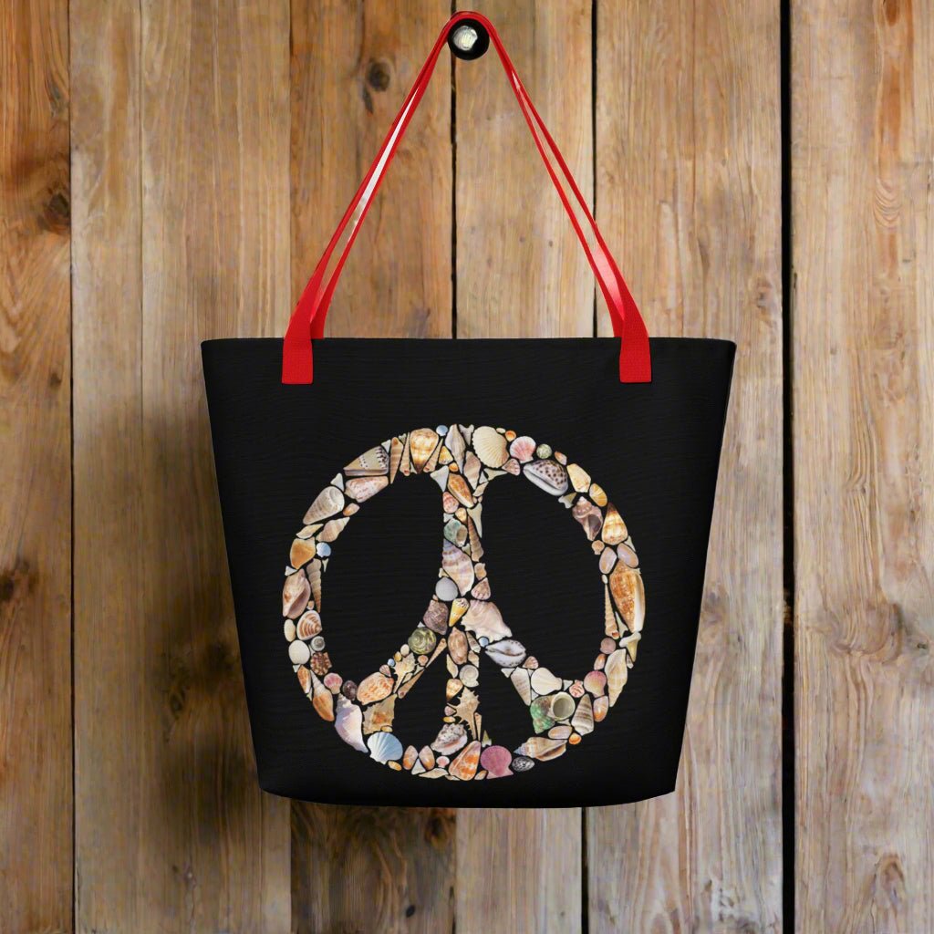 Black Tote Bag with a red strap hanging on a rustic wood wall in a seaside surf shack. Bag features Seashell art forming a Peace Sign