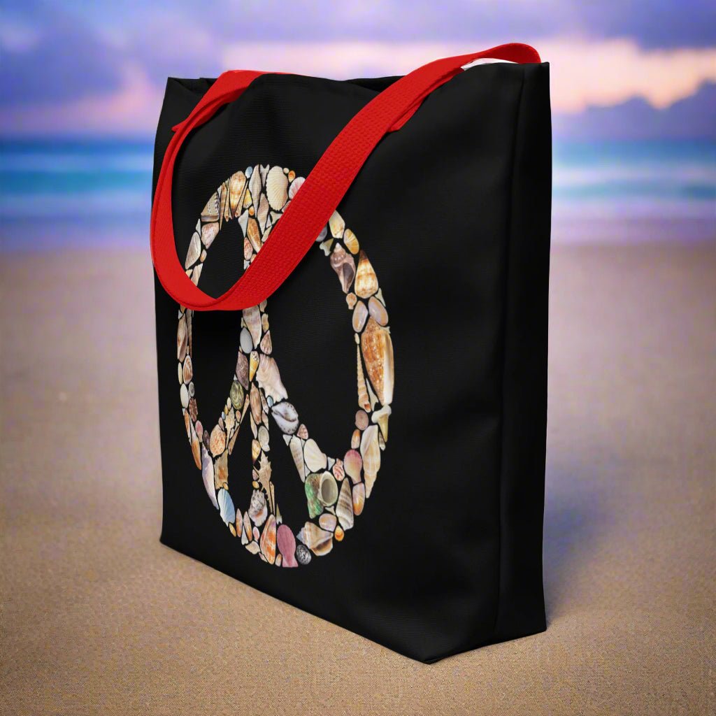 Black Tote Bag with Red Straps featuring a Peace Sign created entirely out of seashells sitting in the sand of your favorite shelling beach