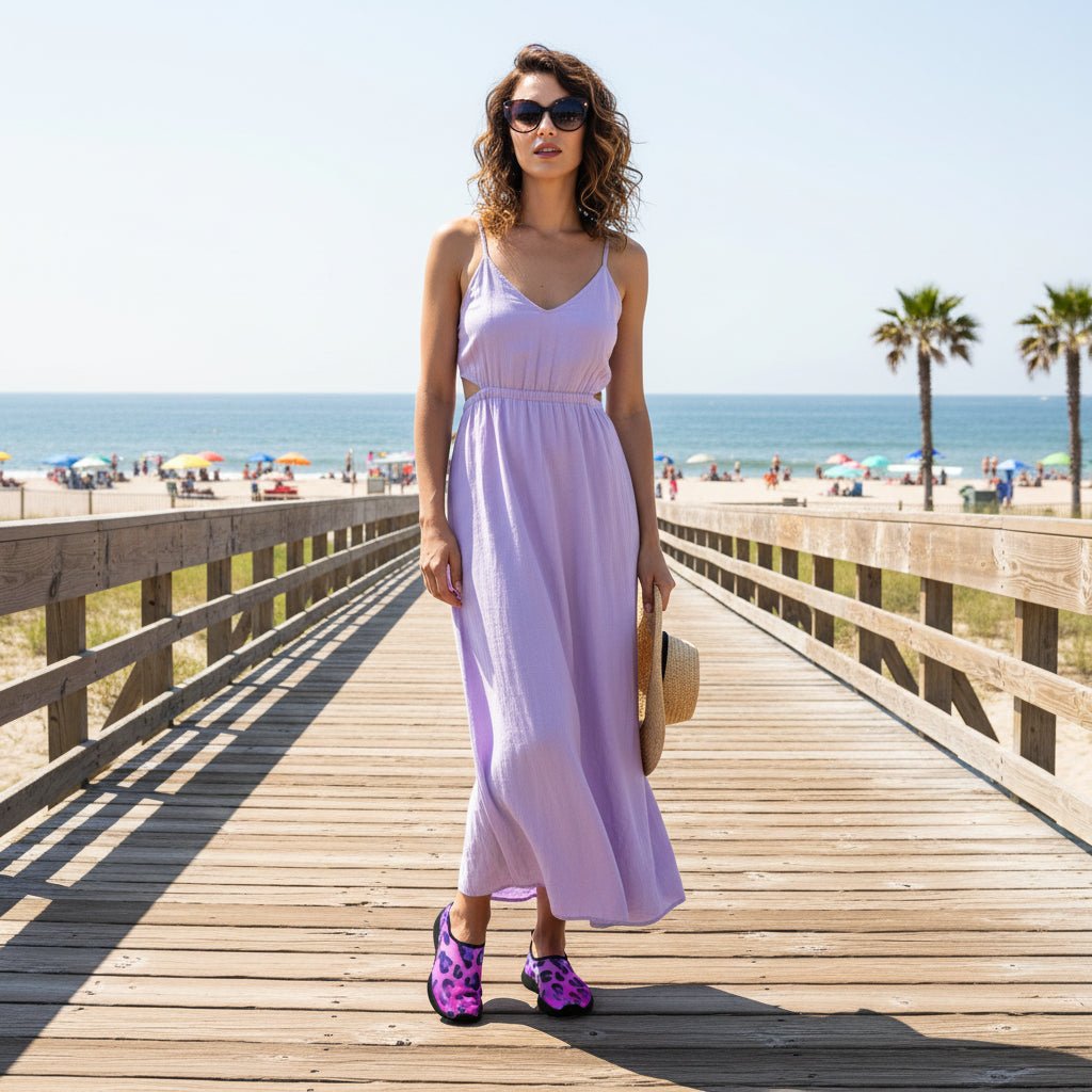 A person standing on a sandy beach boardwalk wearing slip-on water shoes with a bright pink and purple leopard print and black trim.