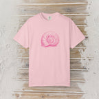 A light pink short-sleeve crewneck t-shirt featuring a pink nautilus shell graphic printed on the chest, displayed flat against a rustic whitewashed wood plank background.