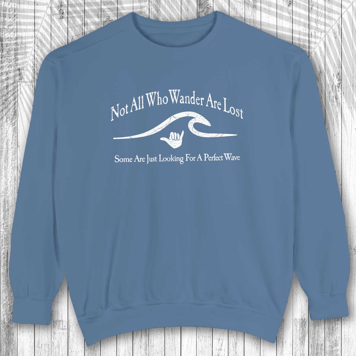 Blue shaka inspired sweatshirt with white text and graphic on a wooden surface
