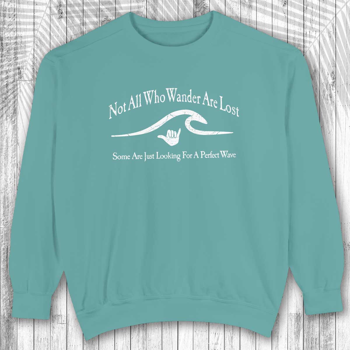 Teal shaka inspired sweatshirt with white text and graphic on a wooden surface