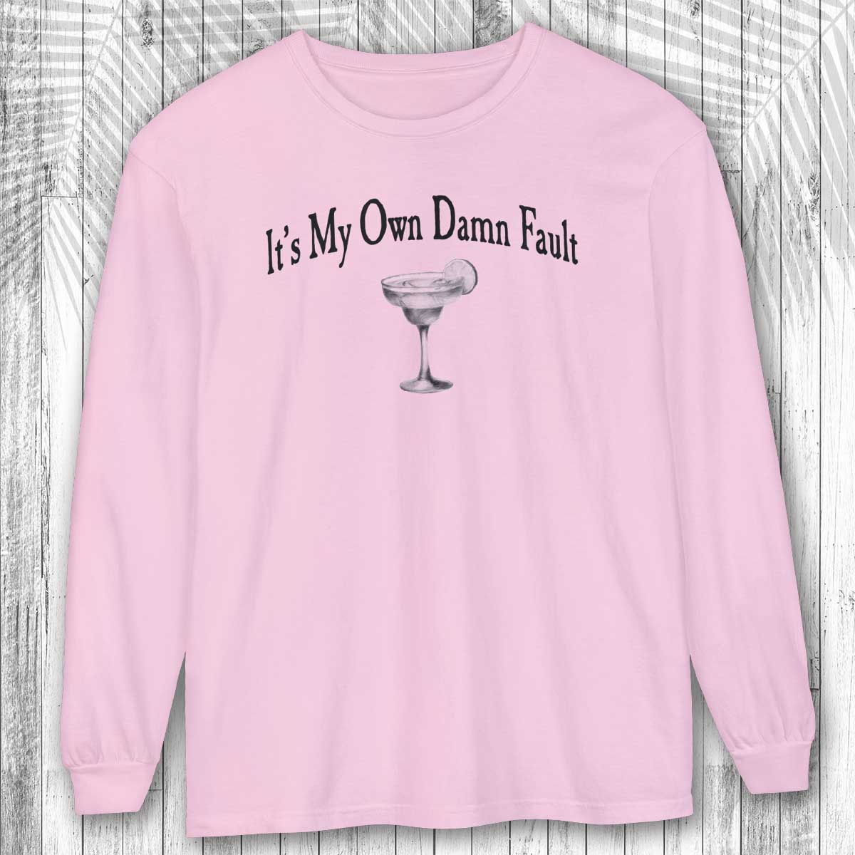 Pink long-sleeve margarita tee shirt with a graphic and text on a wooden surface