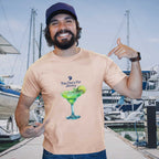 Man wearing a tan t-shirt with a graphic and text, standing in a marina with boats in the background.