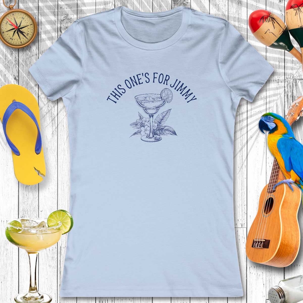 Light blue t-shirt with 'This one's for Jimmy' text and cocktail graphic, surrounded by flip-flops, a guitar, and a parrot.