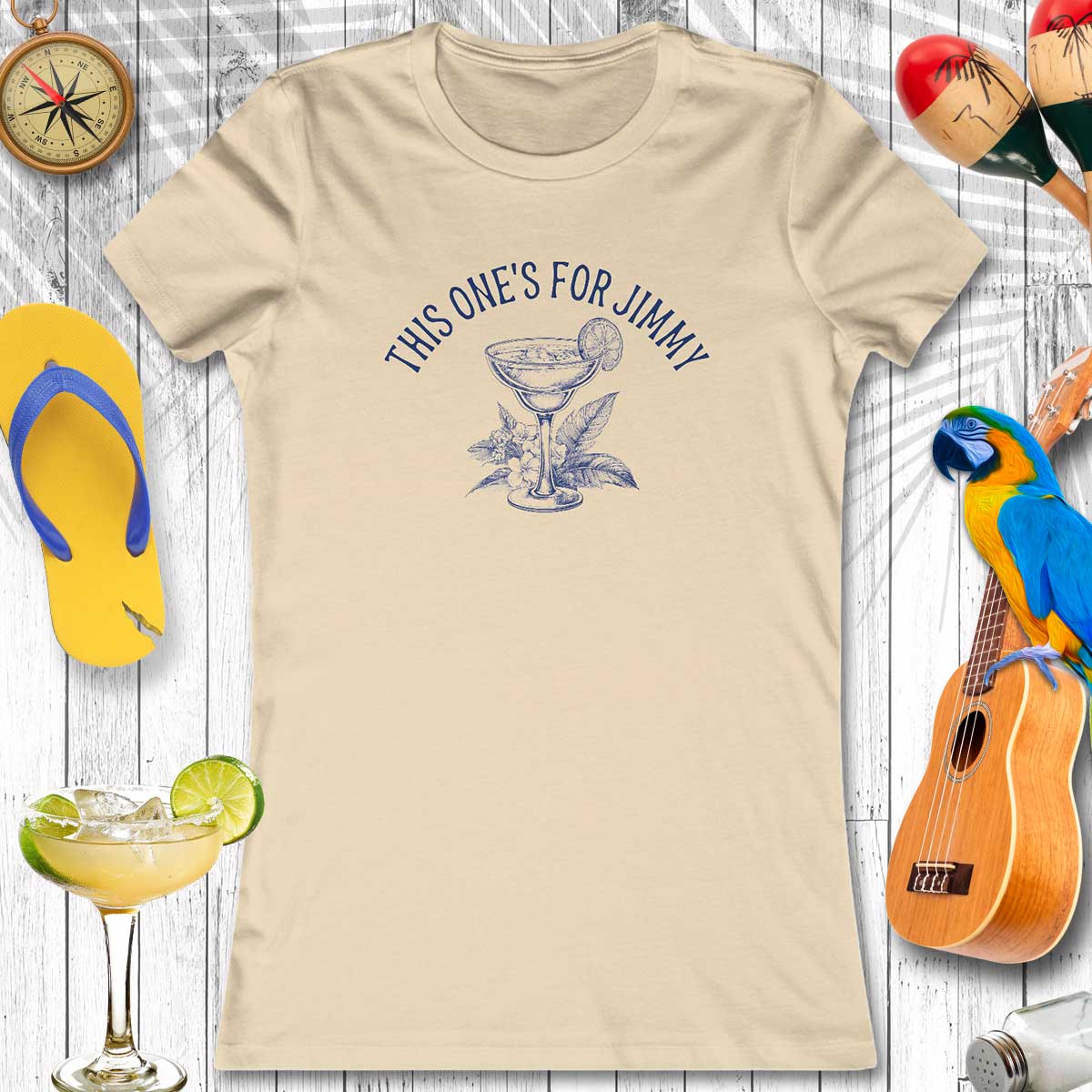 Beige t-shirt with cocktail graphic and text, surrounded by flip-flops, a parrot, and a ukulele on a wooden background.