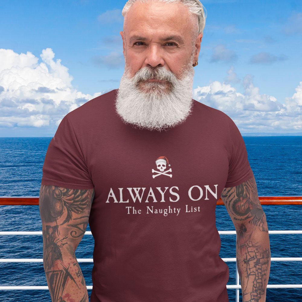 Man wearing a maroon t-shirt with a skull and crossbones design and text, "Always On The Naughty List" standing on a boat with ocean and sky in the background.