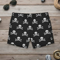 Black swim shorts with white skull and crossbones pattern on a nautical wood background