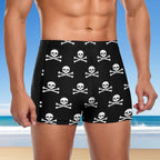 Person wearing black swim shorts with skull and crossbones pattern on a beach.