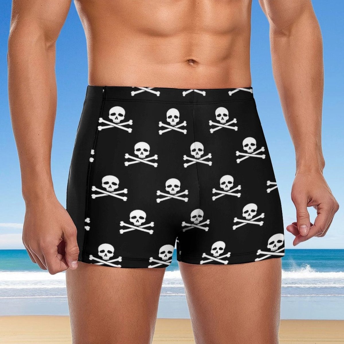 Person wearing black swim shorts with skull and crossbones pattern on a beach.