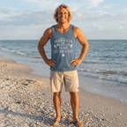 Man standing on a beach wearing a tank top with text and shorts.