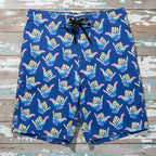 Deep Blue Board shorts with colorful Shaka hand gesture pattern laying flat on a rustic wood deck