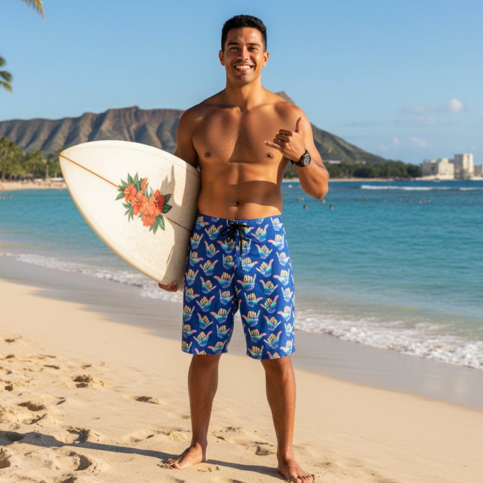 Dude wearing shorts holding a surfboard in one hand and giving the shaka sign with the other on Waikiki Beach