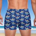 Person wearing blue swim shorts with colorful shaka hand signs pattern on a beach background | Hang Loose