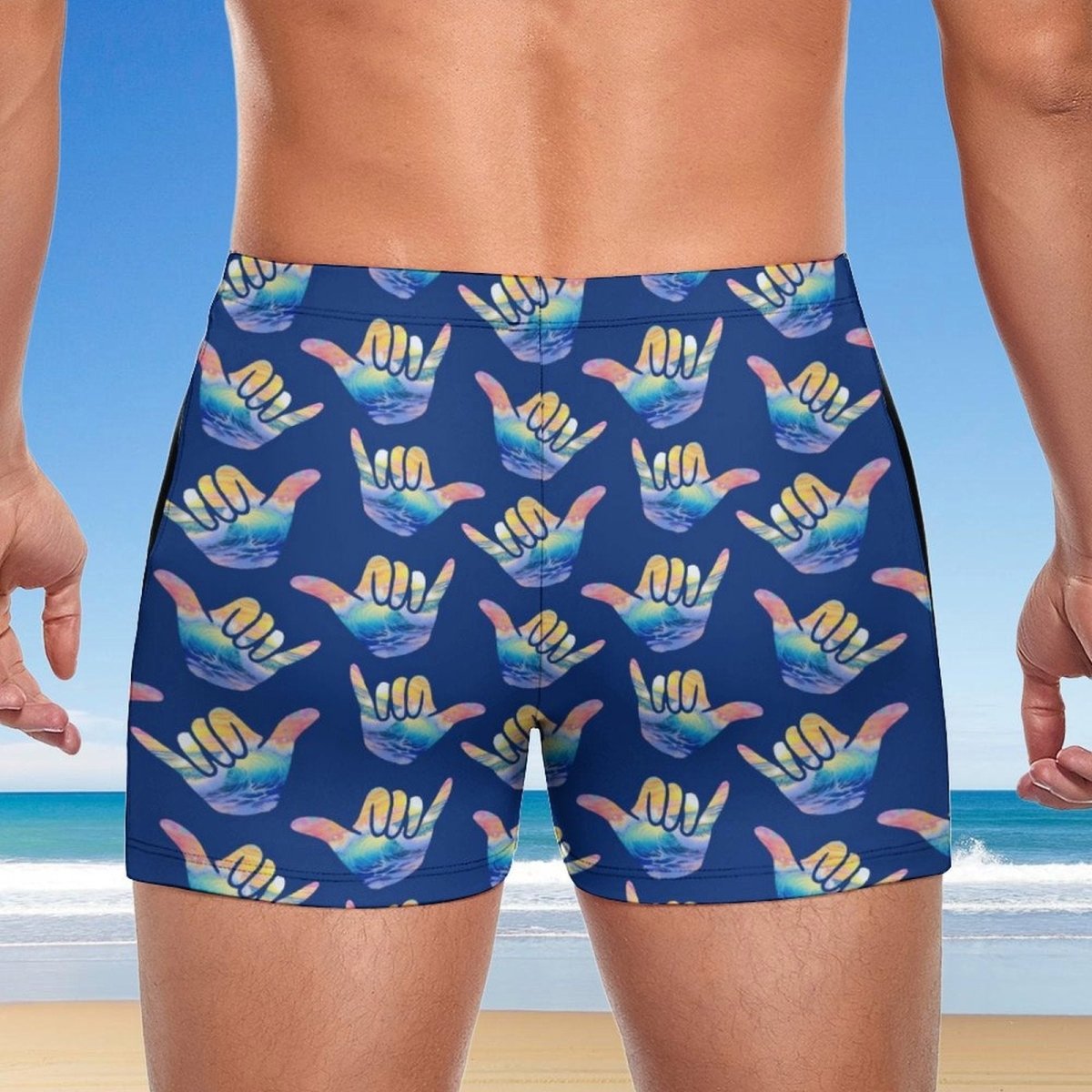 Person wearing blue swim shorts with colorful shaka hand signs pattern on a beach background | Hang Loose