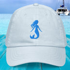 White cap with blue mermaid silhouette on a blue wooden surface with a boat in the background