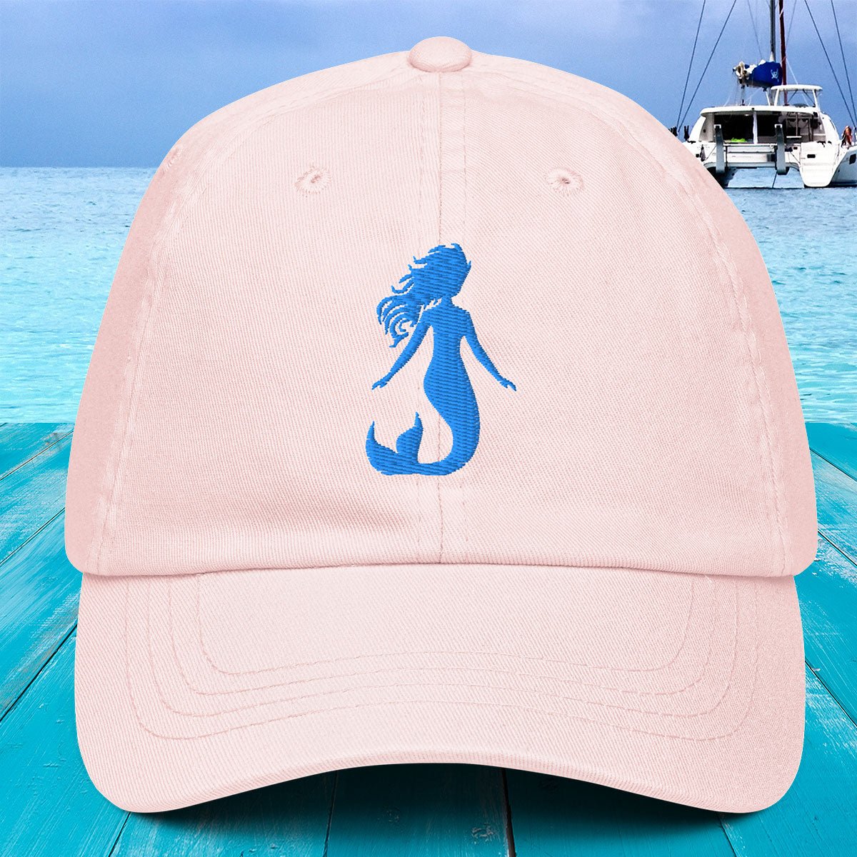 Pink cap with blue mermaid silhouette against a blue water and boat background
