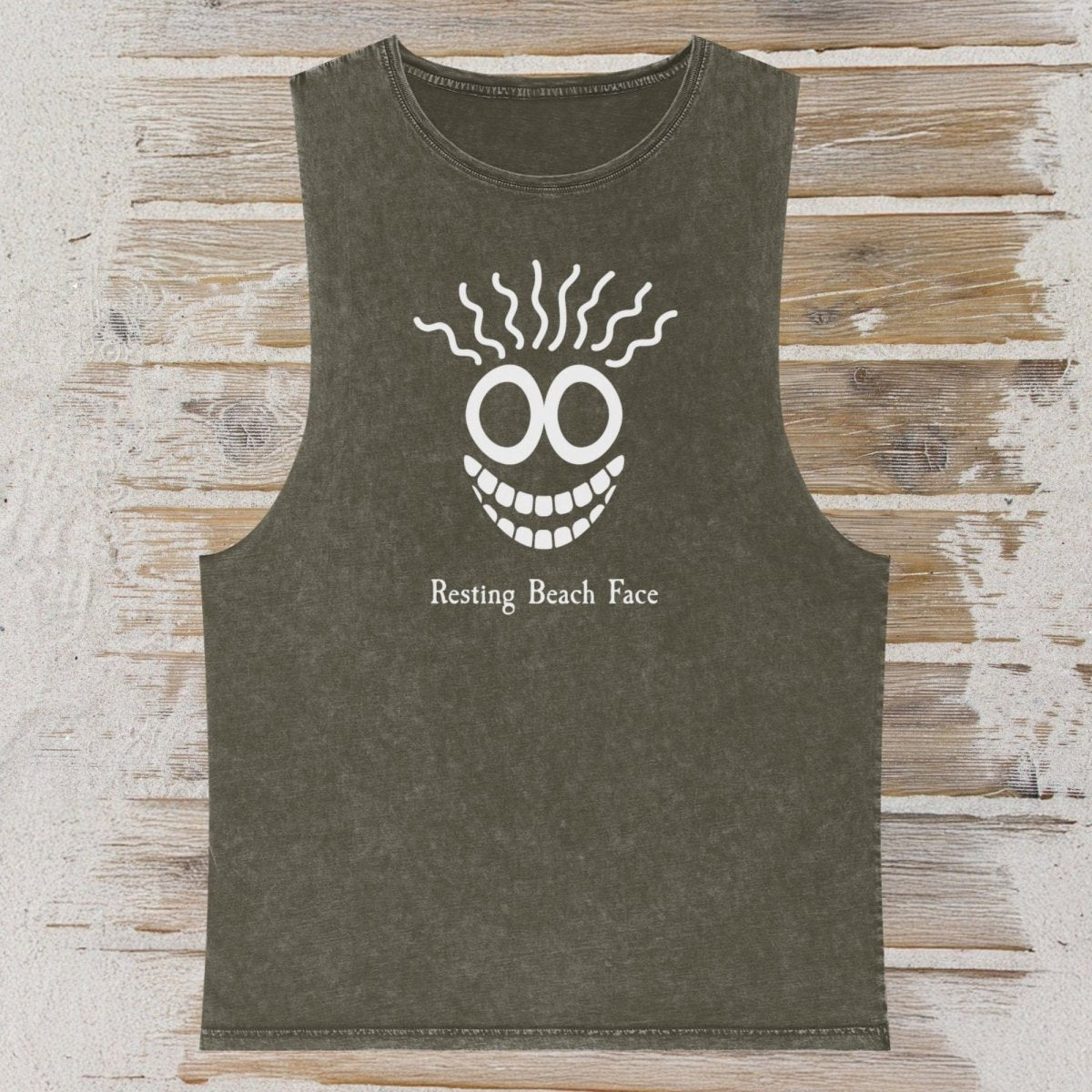 An olive green sleeveless tank top with a white graphic of a smiling face and the text 'Resting Beach Face' printed on the front, displayed flat on a rustic wooden plank background.