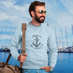 Man wearing a light blue nautical anchor sweatshirt with an anchor design and text, "Always on the nauti list." standing in front of a marina with boats.