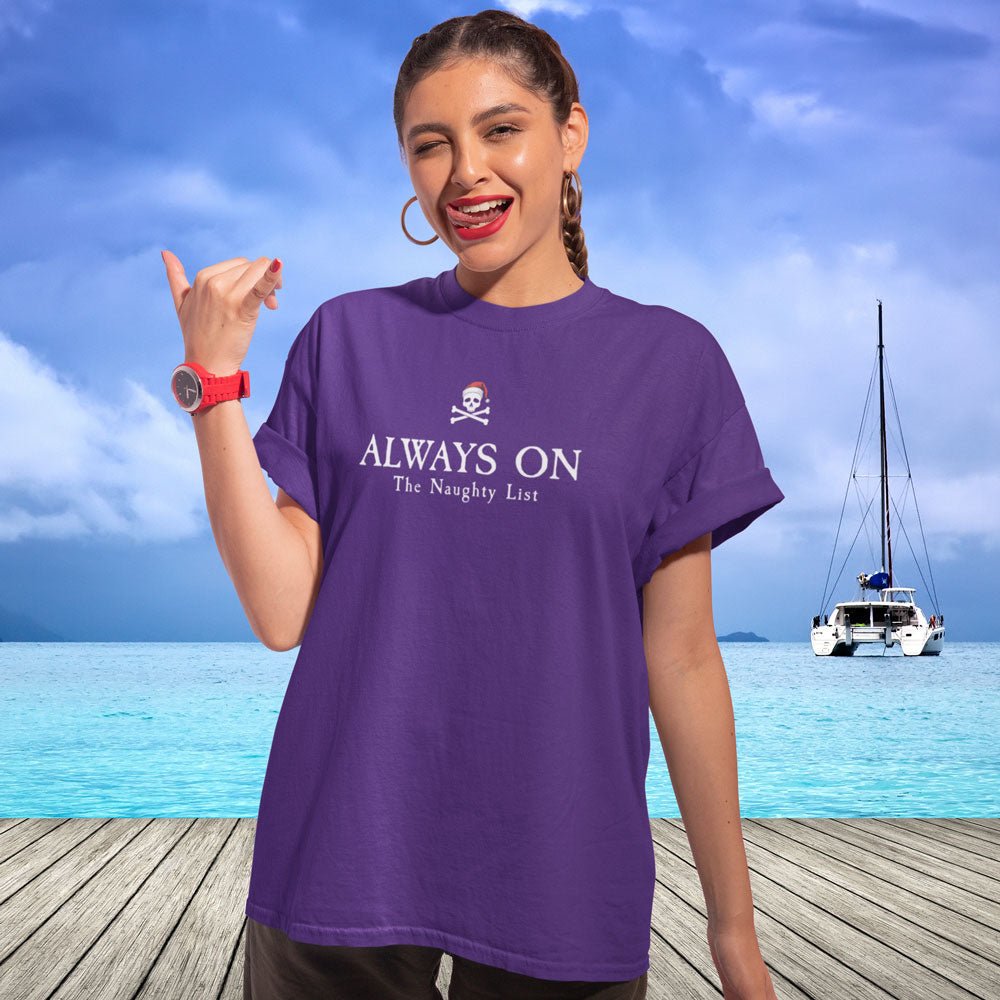 Woman wearing a purple t-shirt with text and a skull icon, standing on a wooden deck with a boat and blue sky in the background.