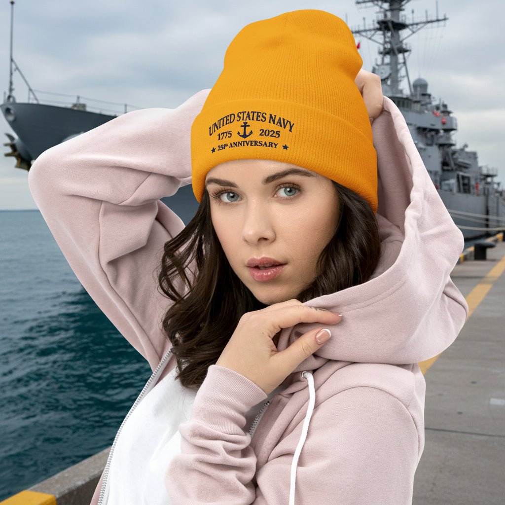 Woman wearing a gold beanie with United States Navy 1775 - 2025 and pink hoodie Navy Pier with a ship in the background
