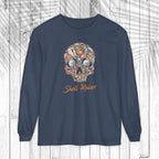 A navy blue long-sleeve t-shirt with a colorful shell skull graphic and the words 'Shell Raiser' printed in orange, displayed on a white wood plank background.