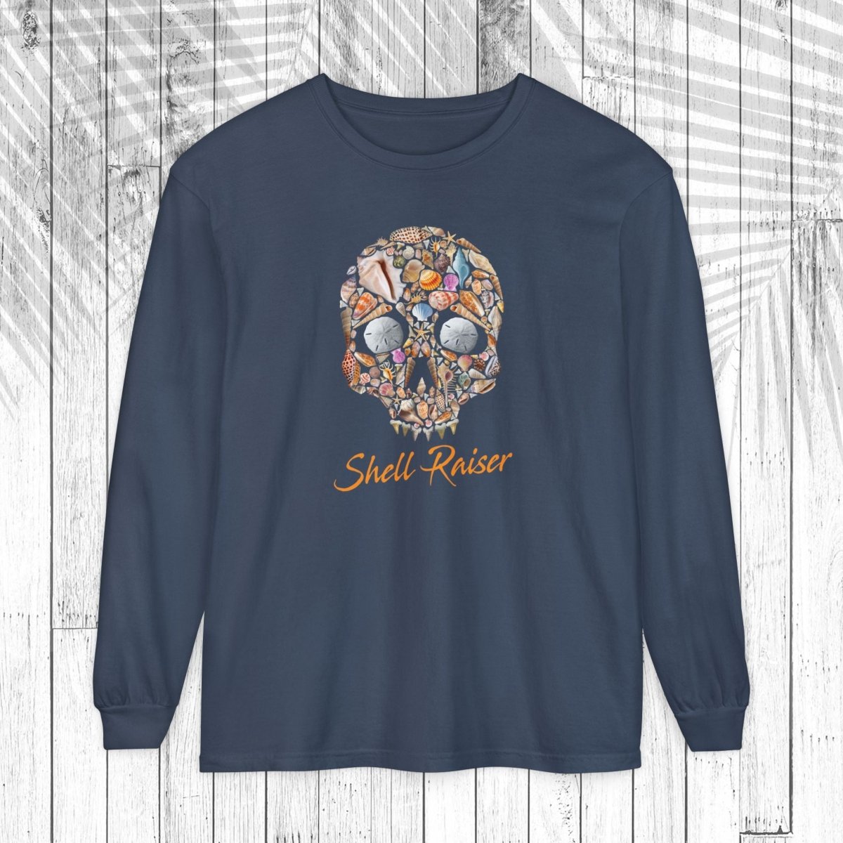 A navy blue long-sleeve t-shirt with a colorful shell skull graphic and the words 'Shell Raiser' printed in orange, displayed on a white wood plank background.