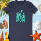 Navy blue Salty Beach Mom tee shirt with coastal design, laid on a beach-themed background with seashells and starfish.