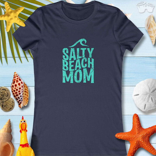 Navy blue Salty Beach Mom tee shirt with coastal design, laid on a beach-themed background with seashells and starfish.