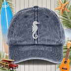 Blue denim cap with a seahorse design on a wooden background with beach elements.