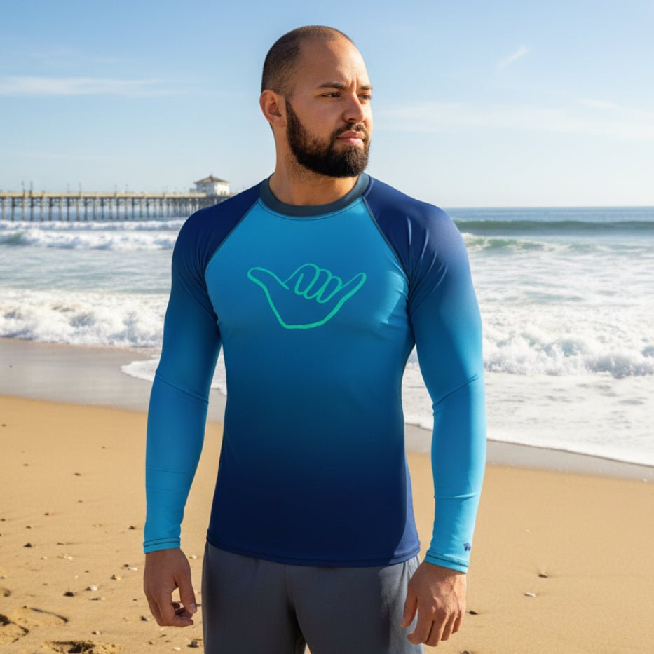 Man wearing a blue long-sleeve rash guard with a shaka sign on Oceanside Beach CA.