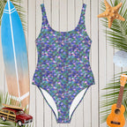 One Piece Mermaid Swimsuit on a rustic wood wall next to a surfboard and a Ukulele. 