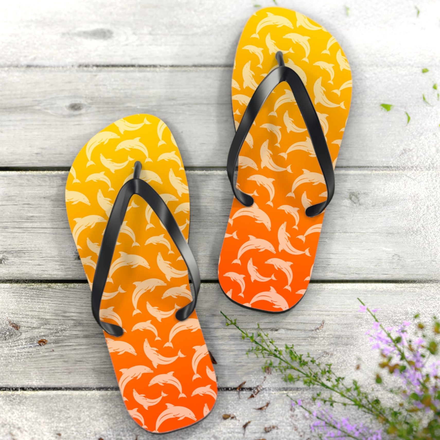 Pair of orange flip-flops with black straps on a wooden surface with flowers.
