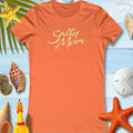 Salty Mom tee shirt in orange with playful script design against beach-themed background.
