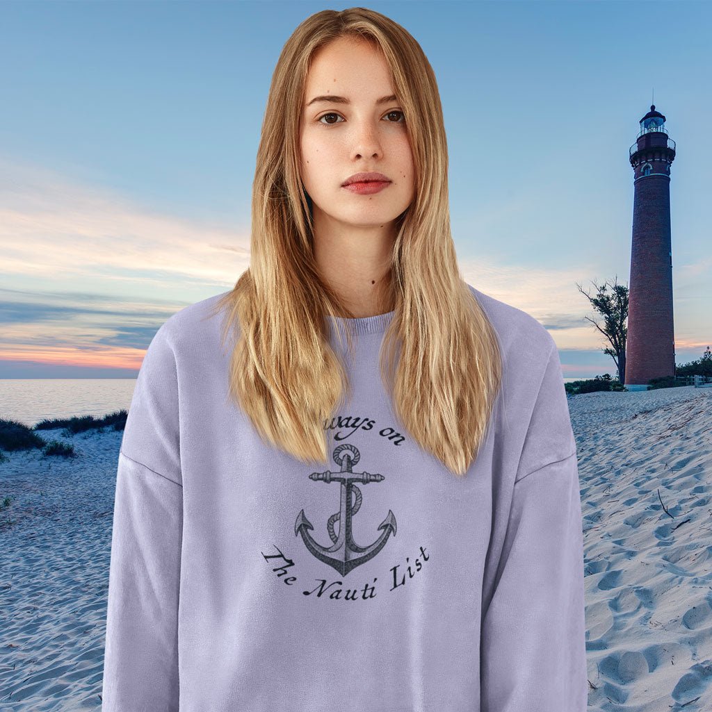 Woman wearing a lavender sweatshirt with an anchor design on a beach with a lighthouse in the background