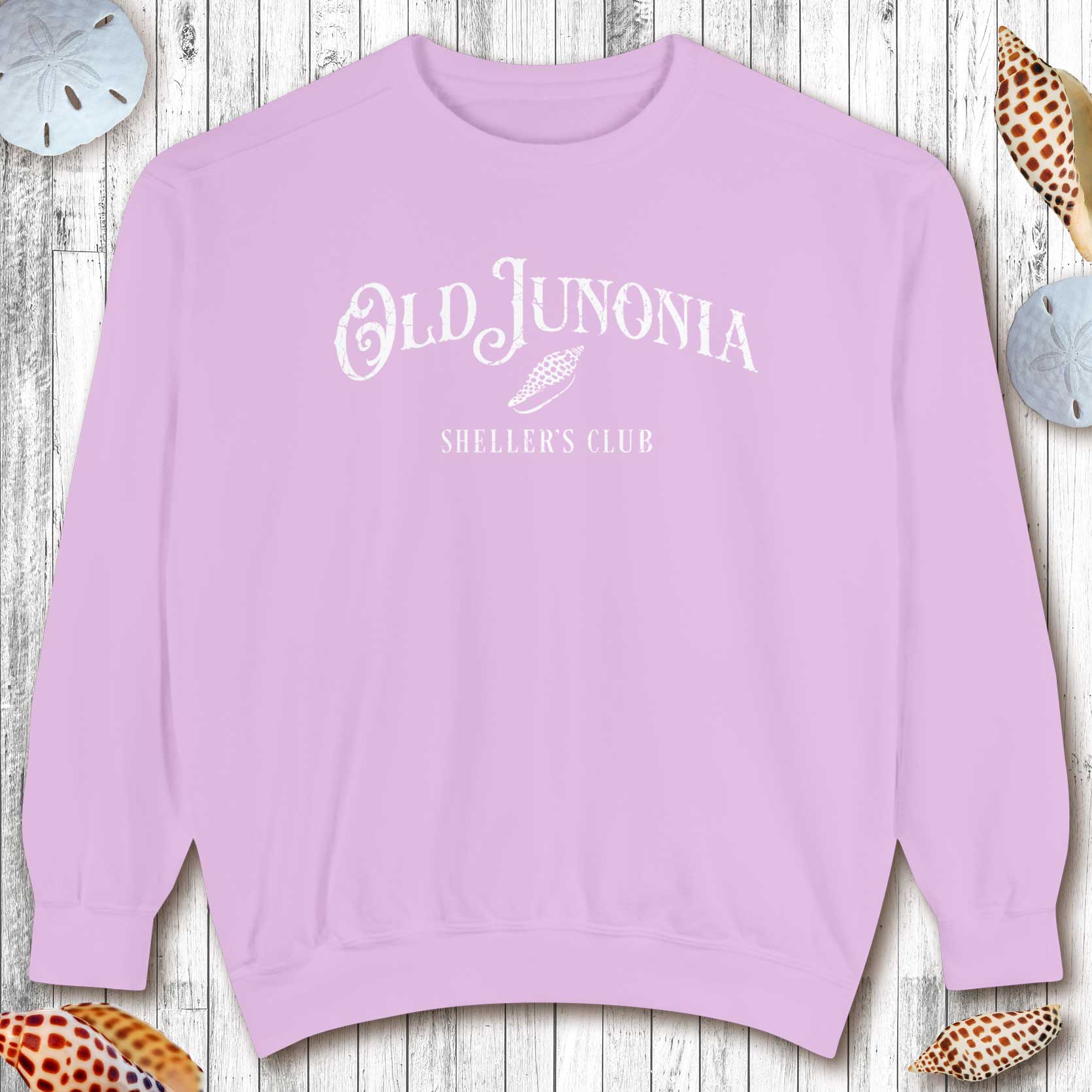 Purple sweatshirt with 'Old Junonia Sheller's Club' text on a wooden surface with seashells.