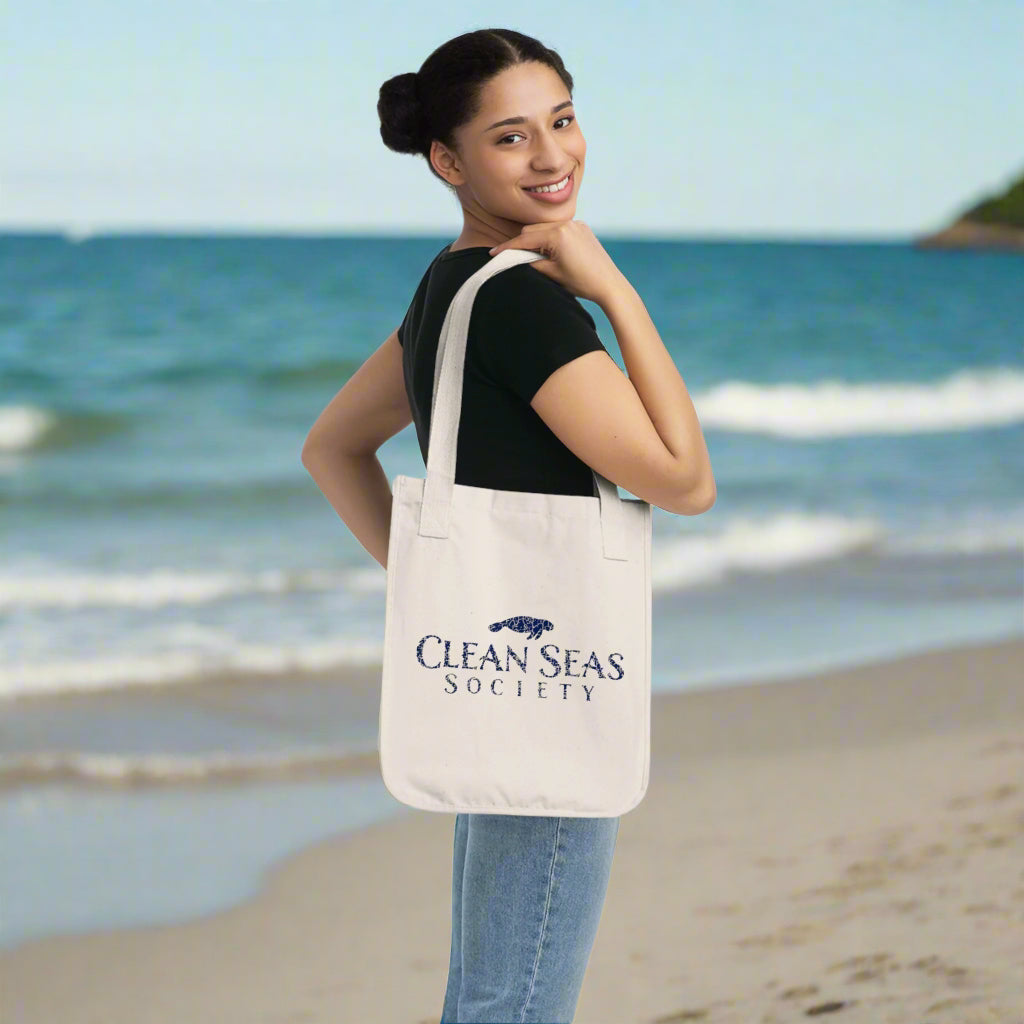 Girl standing on a beach with Organic Canvas Tote Bag with Clean Seas Society logo