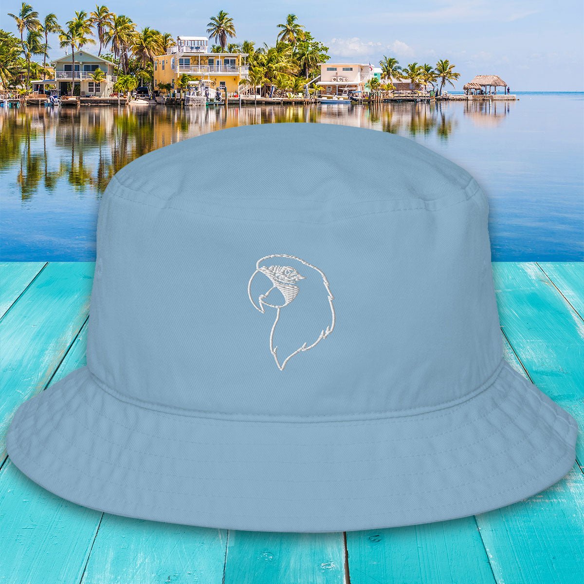Light blue embroidered Parrot Head bucket hat with a logo on a turquoise wooden surface with a tropical background